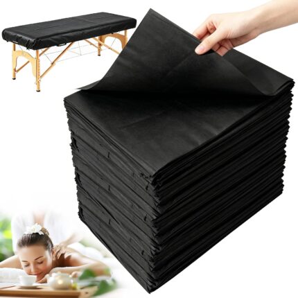 Stack of 100 black disposable massage table sheets, folded neatly, with one sheet partially unfolded on a table.