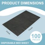 Stack of 100 black disposable massage table sheets, folded neatly, with one sheet partially unfolded on a table.