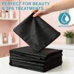 Stack of 100 black disposable massage table sheets, folded neatly, with one sheet partially unfolded on a table.