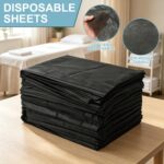 Stack of 100 black disposable massage table sheets, folded neatly, with one sheet partially unfolded on a table.