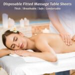 Stack of 30 white disposable fitted massage table sheets with elastic edges, on a spa table.